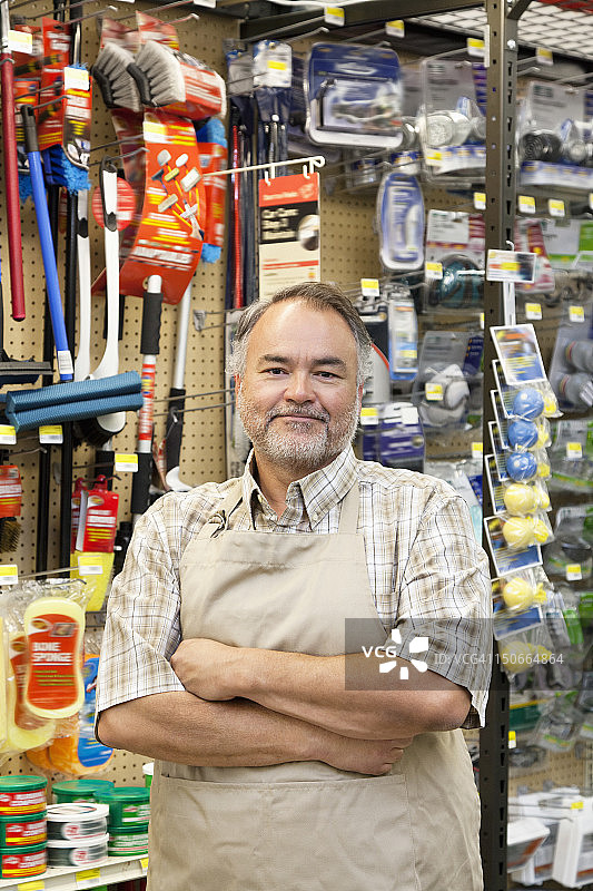 一个自信的成熟的商店职员双臂交叉在五金店的肖像图片素材