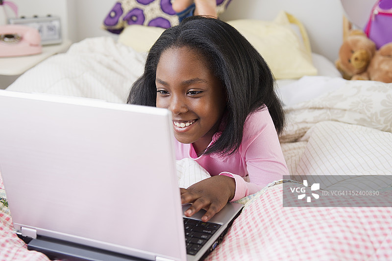 黑人女孩躺在床上用笔记本电脑图片素材