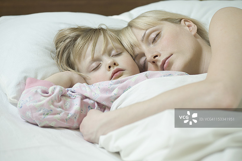 一位母亲和她的小女儿并排睡在一张床上图片素材