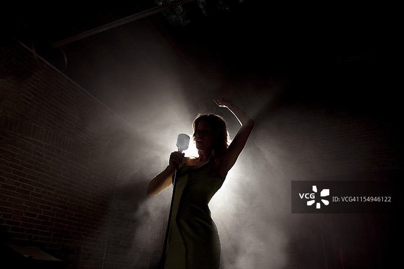 女歌手背光在烟雾缭绕的舞台上图片素材