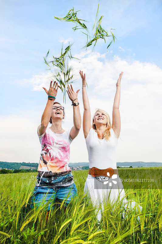 两个年轻的妇女在田里向空中抛谷物图片素材