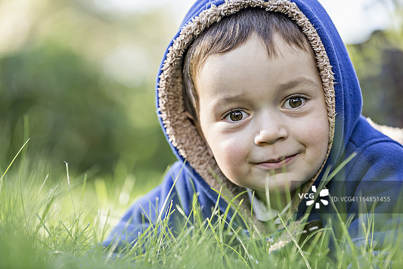 一个穿着兜帽夹克的小男孩在草地上图片素材