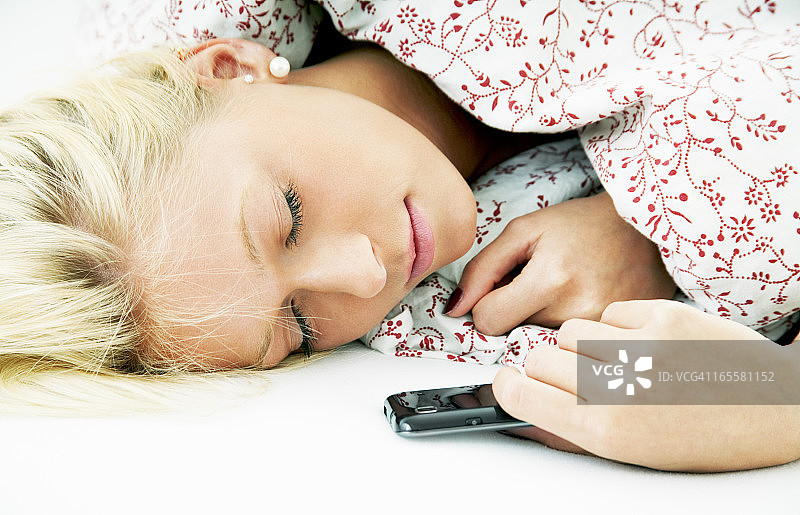 迷人的金发年轻女人睡在床上和智能手机图片素材