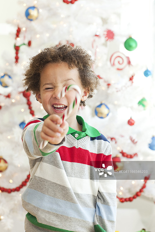 快乐的小男孩与糖果棒摆pose在圣诞树前图片素材