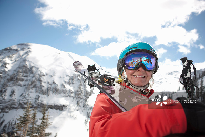 穿着滑雪服的年轻女子把滑雪板举过肩膀，微笑着图片素材