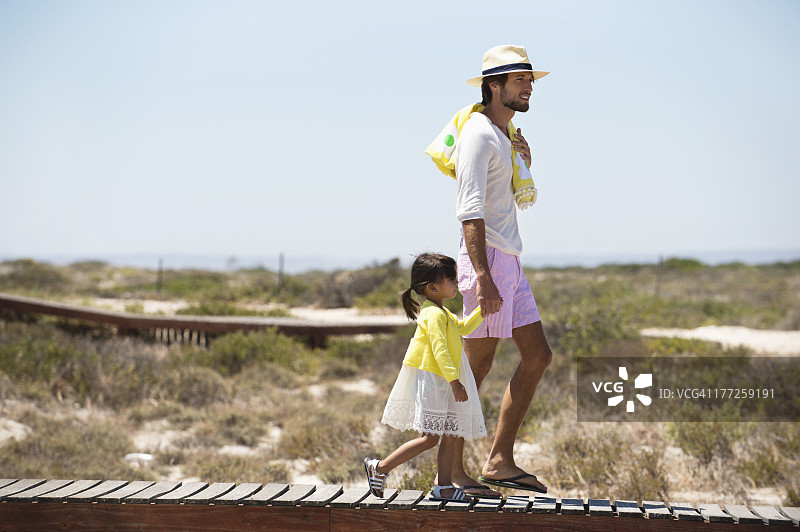 一个男人和他的女儿走在海滩的木板路上图片素材