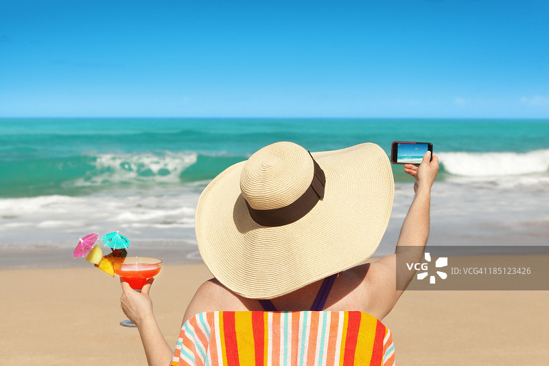 女性游客在暑假用智能手机拍海滩照片图片素材
