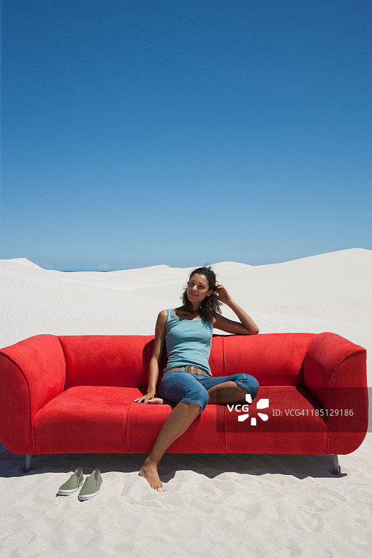 一个女人坐在沙漠中央的红色沙发上图片素材
