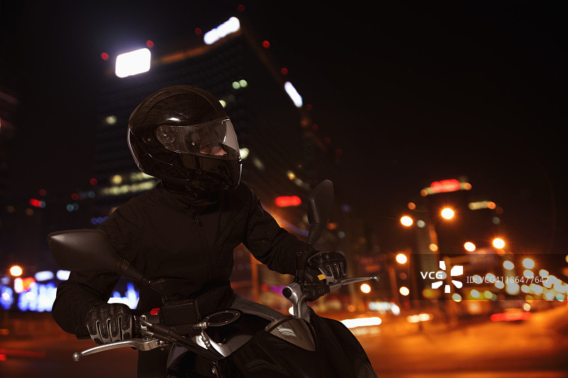 一个年轻人晚上骑着摩托车穿过北京的街道图片素材