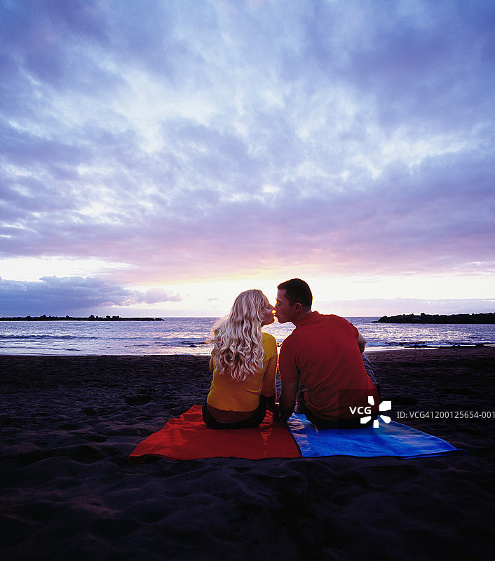 年轻情侣亲吻在海滩上日落，后视图图片素材