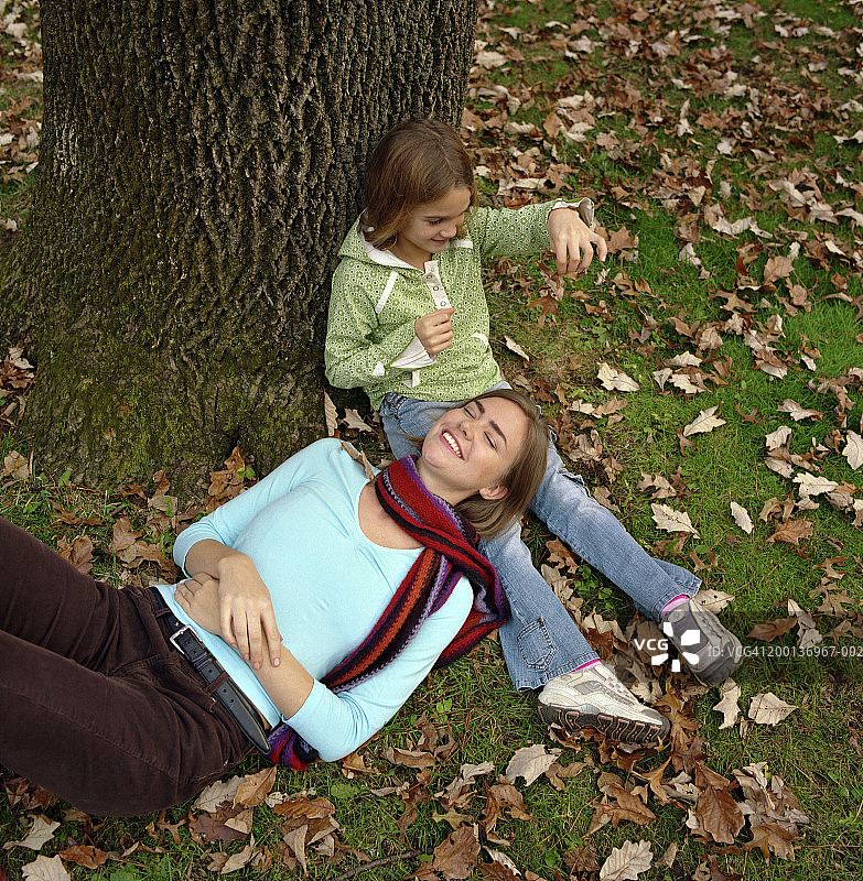 女孩(5-7)在玩树叶，妈妈把头放在女孩的膝盖上，秋天图片素材