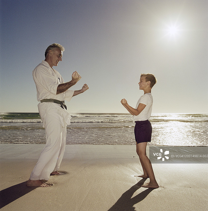 祖父和孙子(8-10)在沙滩上练习空手道，侧视图图片素材
