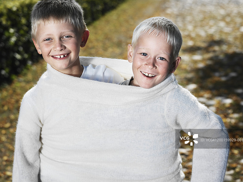 两个男孩(6-8)在户外分享跳绳，微笑，肖像图片素材