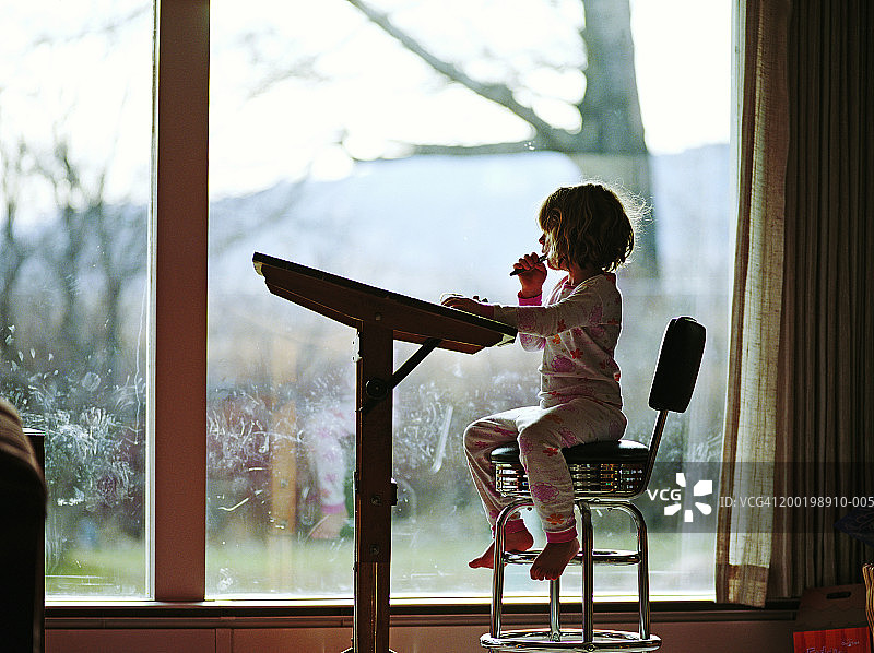 女孩(3-5)在客厅窗户附近的绘画桌旁，侧视图图片素材