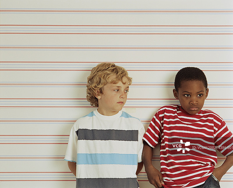 两个男孩(6-8)靠在墙上，皱着眉头，一个看着另一个图片素材