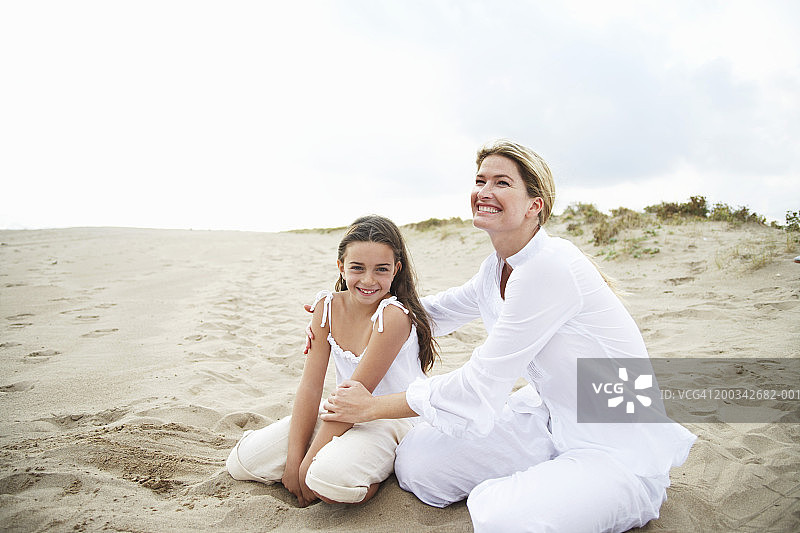母亲和女儿(6-8岁)坐在海滩上，面带微笑图片素材
