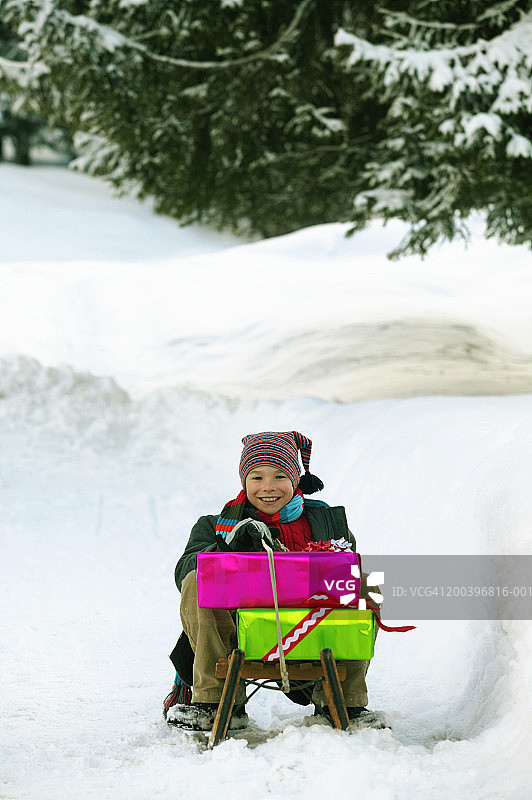 男孩(8-10)坐在雪橇上，带着礼物，微笑着，画像图片素材