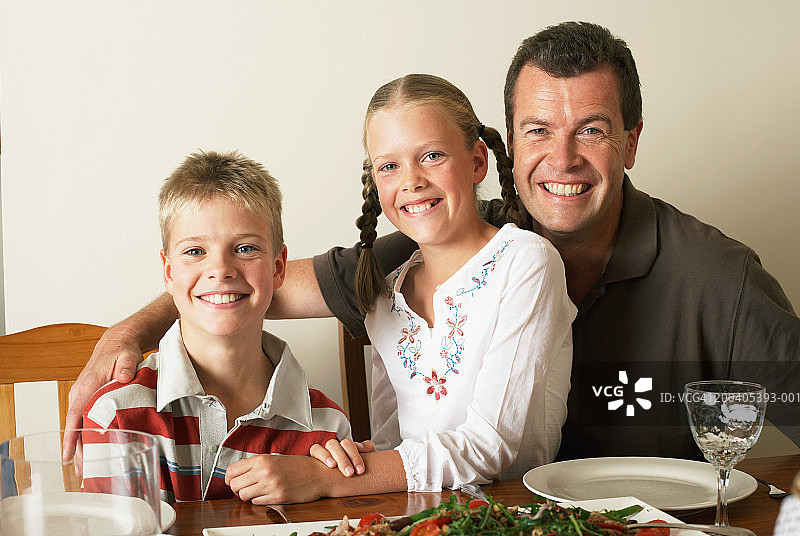 父亲和双胞胎(10-12)在餐桌上，微笑着，肖像图片素材