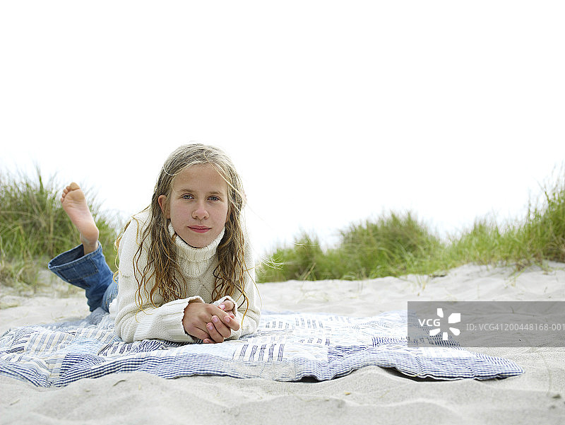 女孩(9-11)躺在沙滩上的毯子上，肖像图片素材