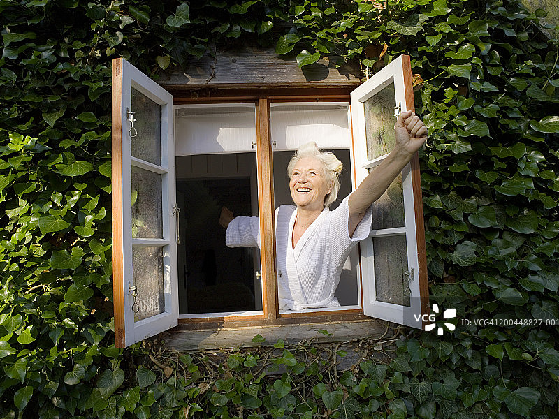 老妇人戴着卷发棒在窗前开窗，面带微笑图片素材