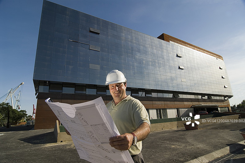 男人在建筑工地上拿着图纸，微笑着，画像图片素材