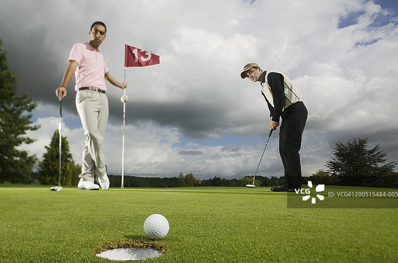 两个人打高尔夫球，高尔夫球在边缘的洞在前景图片素材