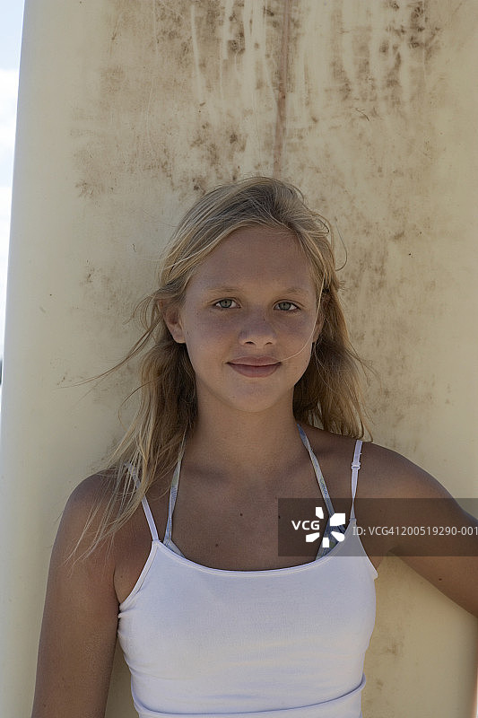 金发女孩(9-11)站在冲浪板旁，微笑着，肖像图片素材