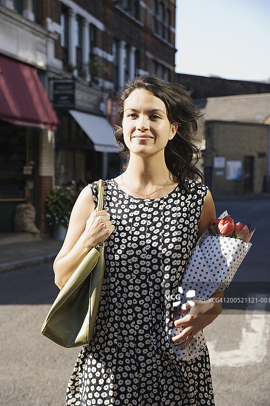 女人站在街上，拿着一束花，画像图片素材