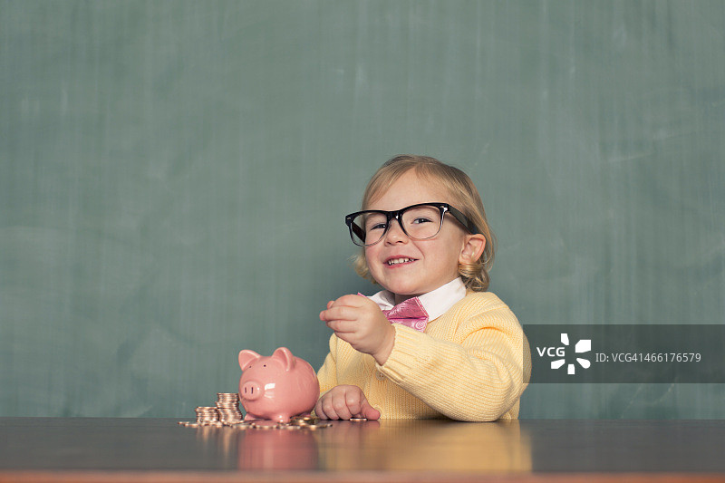 戴眼镜的小女孩在存钱罐里存钱图片素材
