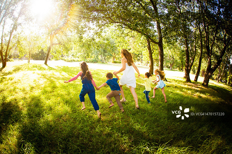 父母和孩子们在阳光明媚的公园里跑步图片素材