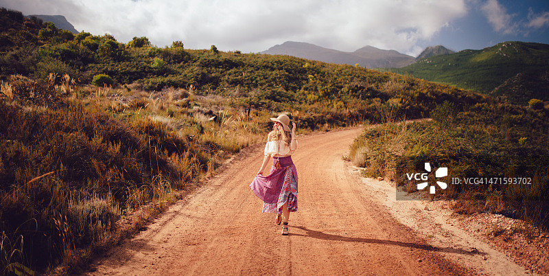 波西米亚女孩走在乡村小路上的自然景观图片素材