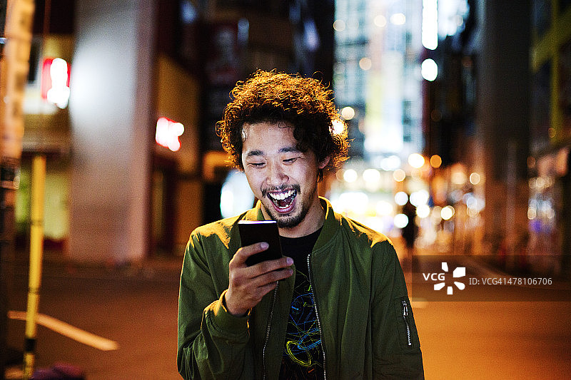 快乐的日本年轻人在晚上使用智能手机，东京。图片素材