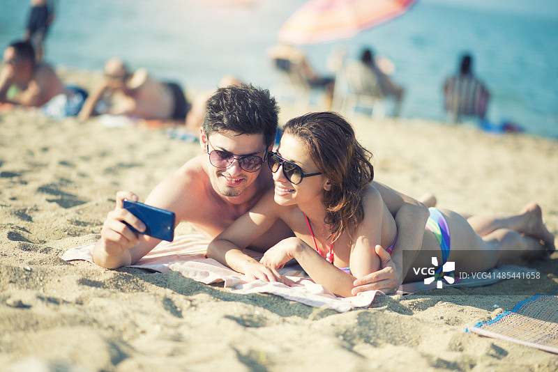 迷人的微笑情侣在海滩上用智能手机自拍图片素材