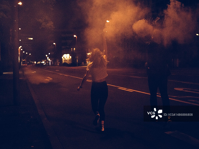 青少年晚上在城市街道上拿着烟雾弹奔跑图片素材