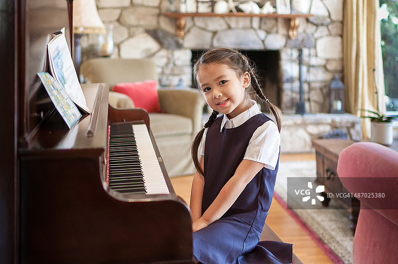 小女孩坐在家里的钢琴前图片素材