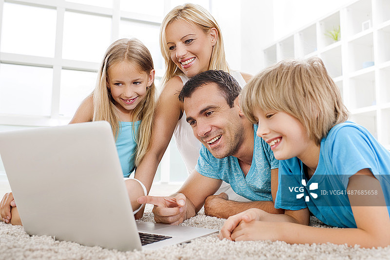 快乐的家庭在家里一起使用笔记本电脑。图片素材