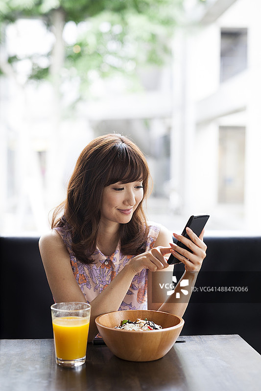 迷人的微笑女孩在自助餐厅使用智能手机图片素材