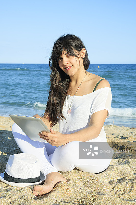 年轻女子在沙滩上拿着平板电脑图片素材