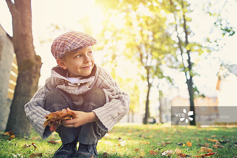小男孩在秋天的公园里捡树叶图片素材
