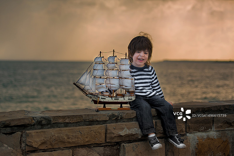 小男孩拿着船玩具，坐在海上玩鞋图片素材