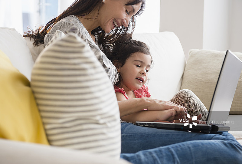 西班牙裔母亲和女儿在沙发上使用笔记本电脑图片素材