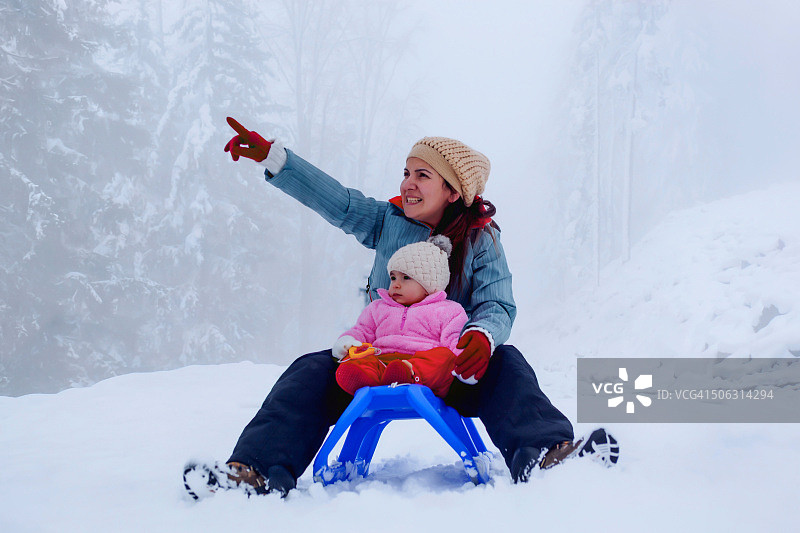 母亲和婴儿女儿享受雪橇图片素材