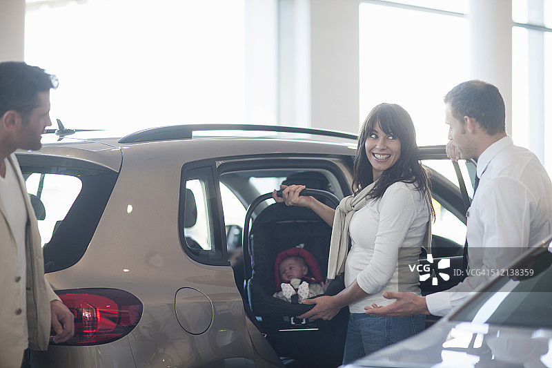 中年成年夫妇带着女儿在汽车经销商试用婴儿座椅图片素材