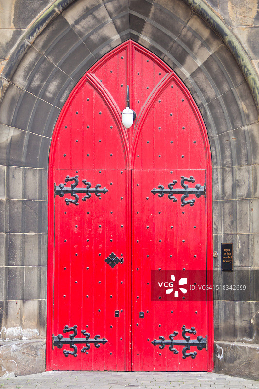 位于苏格兰爱丁堡的哥特式苏格兰圣公会教堂的石拱中，双扇带有黑铁铰链和螺柱的红色木门。图片素材