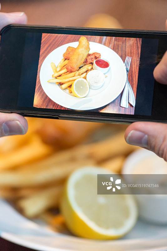 一名男子在餐馆用手机给炸鱼和薯条拍照图片素材