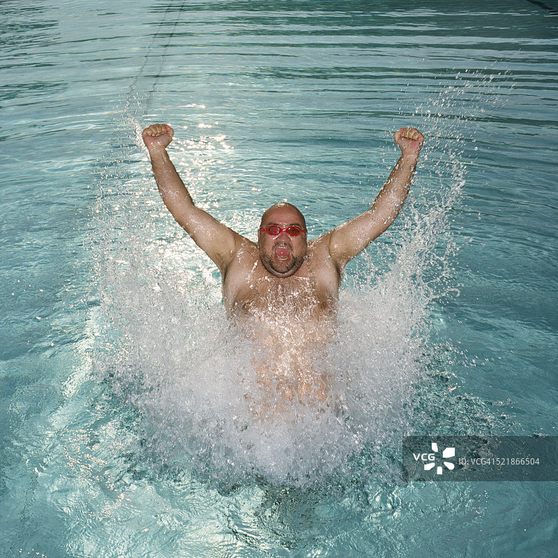 男子在游泳池中跳跃和举起手臂图片素材