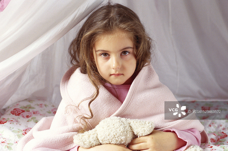 小女孩坐在床上，盖着一条毯子图片素材