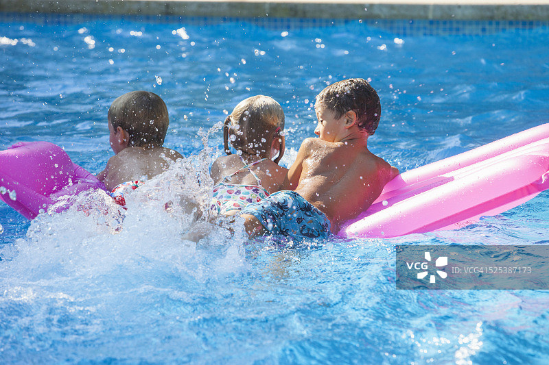 后视图三个孩子玩充气床垫在花园游泳池图片素材