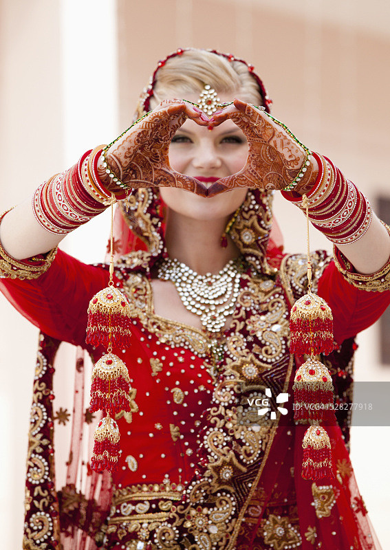 一头金发的新娘，穿着红金色的纱丽，戴着珠宝，双手裹着曼海蒂的图案，做成心形;卢迪亚纳印度旁遮普图片素材