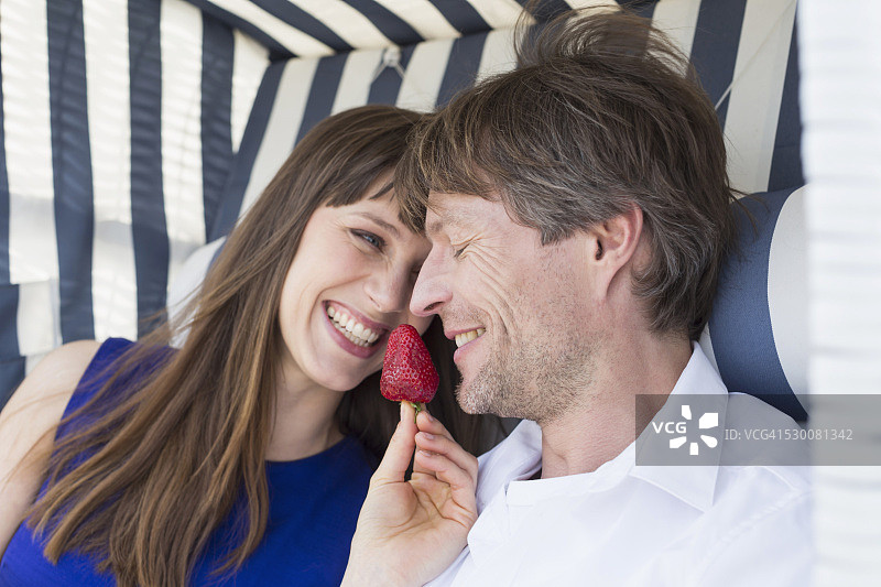 一对夫妇在带屋顶的柳条沙滩椅上微笑着吃草莓图片素材